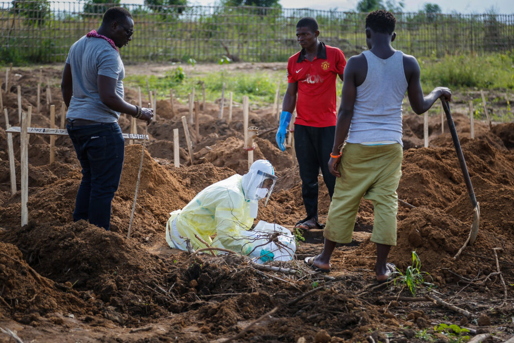 Alfred Kelfala from the roving Freetown Ebola burial team, wearing a head-to-toe  protective suit,  carefully lowers the corpse of a small child into its grave.